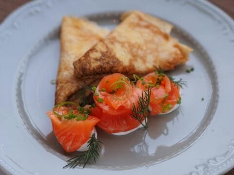 Plate of crepes served with smoked salmon roses, fresh dill, and cream, presented on a white dish—low-carb breakfast without eggs.