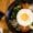 Korean bibimbap served in a black bowl with white rice, sautéed vegetables, minced meat, and a sunny-side-up egg on top, placed on a wooden table.