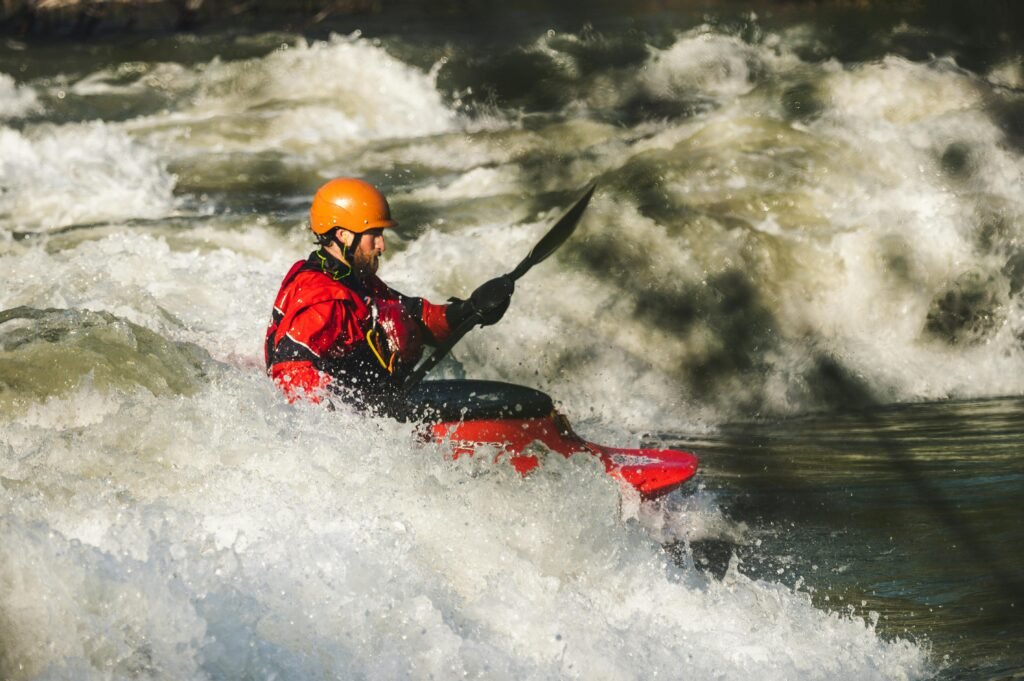 10 Adventure Travel Destinations to Test Your Limits in 2025 4 Man kayaking through intense white-water rapids, wearing a red jacket and orange helmet, showcasing an extreme adventure activity in a wild river setting.