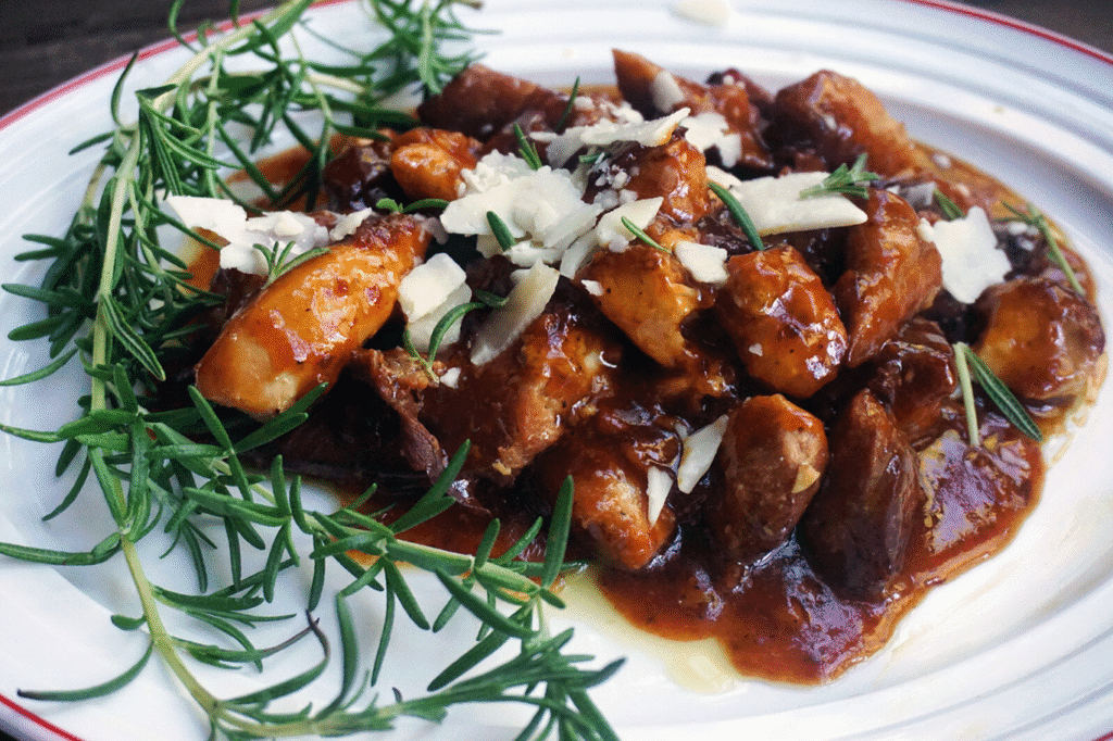 Slow-cooked meat in rich sauce topped with cheese and rosemary