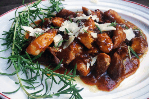 Slow-cooked meat in rich sauce topped with cheese and rosemary
