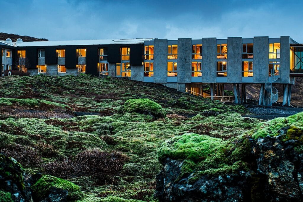 8 Best Hotels In Iceland That Will Exceed Your Expectations 4 Modern hotel building in Iceland surrounded by moss-covered lava fields under a dramatic evening sky.