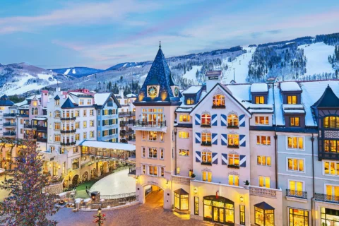 Snow-covered alpine-style resort buildings in Vail, Colorado, with ski slopes and pine trees in the background