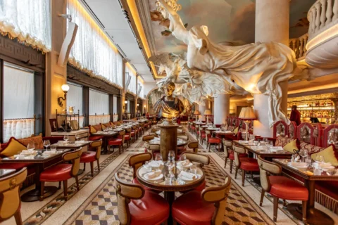 Elegant dining room of a London restaurant with classical statues, ornate ceilings, red leather chairs, and intricately tiled floors.