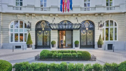 Alt text: Elegant entrance of the Mandarin Oriental Ritz Madrid featuring ornate iron gates, flags, and a uniformed doorman welcoming guests.