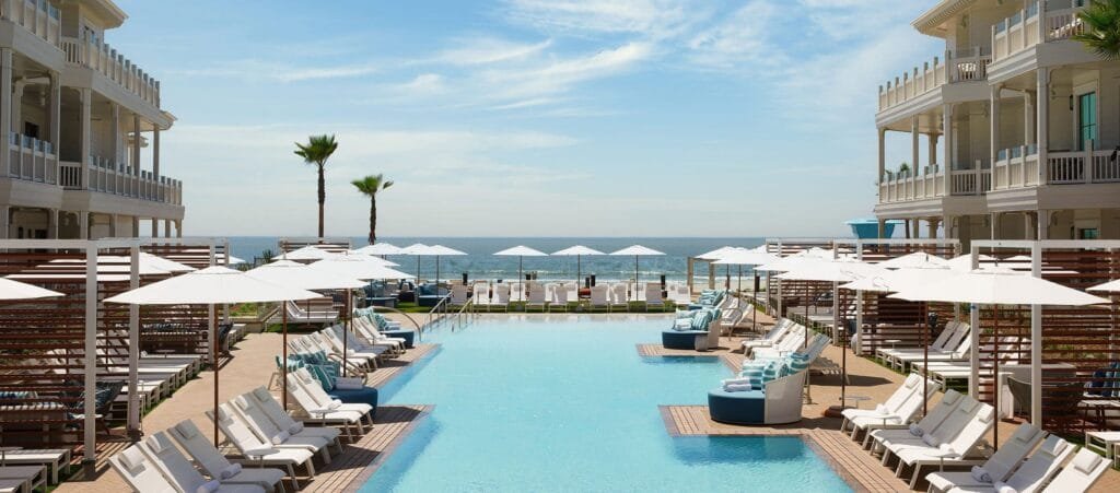 Luxury beachfront resort in San Diego featuring a large ocean-facing pool, white lounge chairs, cabanas, and palm trees under a clear blue sky
