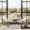 Elegant hotel room interior with two lounge chairs and a table facing large floor-to-ceiling windows, offering a panoramic view of a historic Parisian street, bridge, and classic buildings along the Seine River.