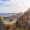 View from the Acropolis of Lindos in Rhodes, Greece, showing ancient temple ruins perched on a rocky cliff overlooking a turquoise bay and the vast Aegean Sea under a partly cloudy sky.