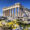 The Parthenon atop the Acropolis in Athens, Greece, viewed from a rocky foreground with blooming yellow wildflowers under a clear blue sky.