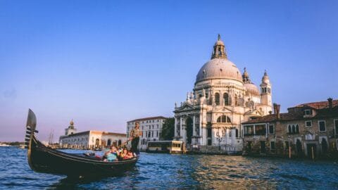 Where to Visit in Italy for the First Time? 29 Gondola gliding through the Grand Canal in Venice at sunset, passing by the iconic Basilica di Santa Maria della Salute.