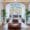 Elegant common area in a Barcelona hostel with large windows, vintage wooden floors, indoor plants, and cozy lounge seating including leather chairs and a bean bag.