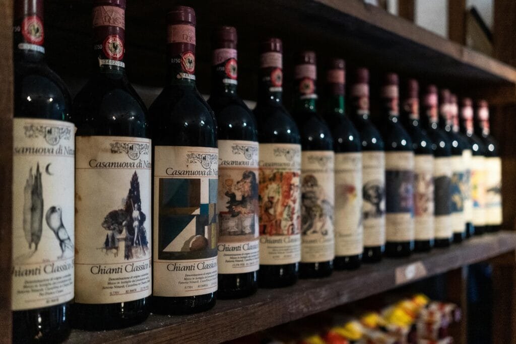 7 Best Wine Tasting in Italy for Passionate Wine Lovers 4 A row of Chianti Classico wine bottles from Casanuova di Nittardi displayed on a rustic wooden shelf in an Italian wine cellar.
