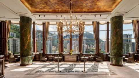Luxurious hotel lounge in Hong Kong with chandeliers, marble columns, and panoramic city and mountain views through floor-to-ceiling windows.
