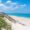 Wooden staircase leading to a white sandy beach with clear blue water under a bright sky.